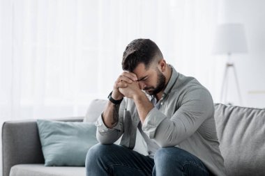 Mutsuz, bunalımlı, ağlayan beyaz bir erkek. Oturma odasında yüzünü kapatıyor. Çaresiz ve yalnız hissediyor. İş stresi, işsizlik, endişe, kalp kırıklığı ve depresyon