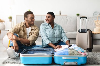 Aile tatili. Afro-Amerikalı çift bavullarını topluyor. Evde otururken gülümsüyorlar. İyi Gezginler Yolculuk İçin Hazırlık Poz Veriyor. Turizm ve Seyahat Konsepti