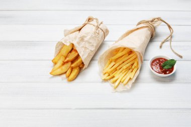 Patates dilimleri ve patates kızartması kahverengi ambalaj kağıdına sarılmış. Fast food beyaz eski şık ahşap götürmek. Domates soslu kızarmış patates. Cips, patates dilimleri. Üst görünüm, copyspace ile düz yatıyordu