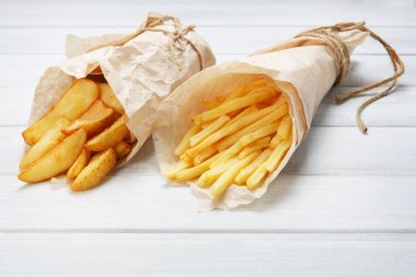 Patates dilimleri ve patates kızartması kahverengi ambalaj kağıdına sarılmış. Fast food beyaz eski şık ahşap götürmek. Domates soslu kızarmış patates. Cips, patates dilimleri. Üst görünüm, düz döşeme, yakın çekim.
