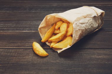 Kahverengi kraft ambalaj kağıdına sarılmış lezzetli patates dilimleri. Fast food alır. Rustik ahşap tahtalar arka planda kızarmış patates. Ağaçta patates. Kızarmış cips, patates dilimleri. Üst görünüm, yumuşak ton