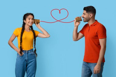 İki genç insan, kalp şeklini oluşturan kırmızı bir telle birbirine bağlı olan teneke telefonları kullanarak bir anı paylaşıyor..