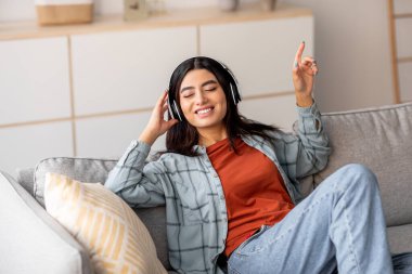 Bin yıllık Arap bir kadın, gözleri kapalı kanepede dinlenirken müzik dinliyor. Kulaklık takıyor ve gülümsüyor. En sevdiği şarkı listesine dalmış..