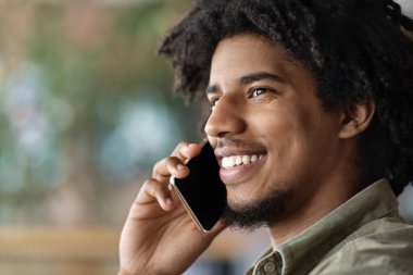 Bin yıllık neşeli Afro-Amerikan kıvırcık saçlı adam kafenin içinde akıllı telefonla konuşuyor. Profili yakın, kırpılmış. Arkadaş veya istemciye çağrı, uzaktan ve modern teknoloji, serbest alan