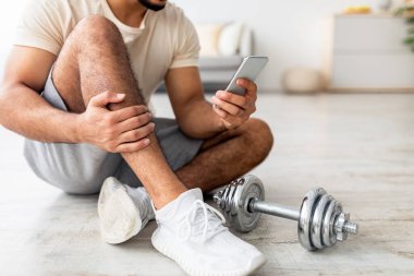 Dambıl egzersizinden sonra akıllı telefonuyla yerde oturan genç bir Arap 'ın görüntüsü internetteki yeni spor videolarına bakıyor. Tanımlanamayan milenyum elemanı ev içi eğitimden sonra ara veriyor, boşluğu kopyalıyor