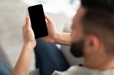 Evdeki koltukta akıllı telefon kullanan tanınmayan genç bir Arap. Uygulama ya da web sitesi tasarımı için model alıyor. Millennial Eastern elemanı elinde kopyalama alanı olan mobil bir cihaz tutuyor, çalışıyor ya da çalışıyor