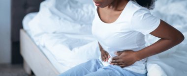 Bir kadın kederli bir ifadeyle yatağında oturuyor, karnını tutuyor. Mide ağrısıyla mücadelesini yansıtan bir rahatsızlığı var gibi görünüyor. Sabahları yatak odası oluyor..