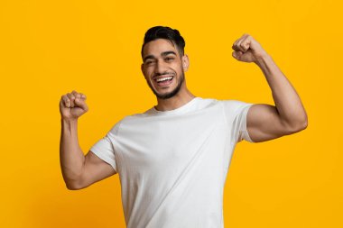 Neşeli atletik ortadoğu milenyumu adamı sarı stüdyo geçmişi üzerinde kaslarını gösteriyor eğitim için egzersiz programı öneriyor Arap adam başarıyı kutluyor, boşluğu kopyalıyor.