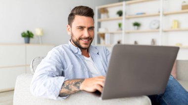 Kanepede dizüstü bilgisayarı, panoraması, fotokopisi olan olumlu bir adam. Yakışıklı adam defter kullanıyor, film izliyor, internette sörf yapıyor ya da sosyal ağlarda geziniyor.