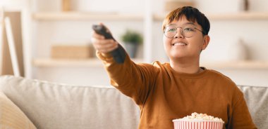 Oturma odasındaki koltukta oturan biri uzaktan kumandayı tutuyor ve gülümsüyor. Yakınlarda bir kase patlamış mısırları var ve ekrana odaklanmışlar. Filmlerinin tadını çıkarıyorlar..