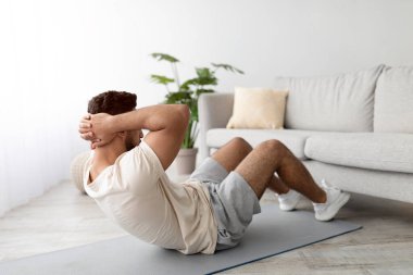 Atletik genç Arap adam evde, koltuğun yanında kaslarını çalıştırıyor. Milenyum Orta Doğulu sağlıklı yaşam tarzını sürdüren, salgın sırasında spor yapan, ev ortamında spor yapan,