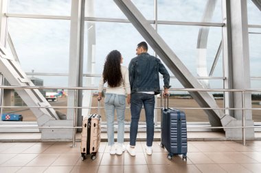 Yeni evliler için seyahatler. Havaalanı Terminali 'nin penceresinin yanında duran genç Arap eşlerinin arka görüntüsü, bavulları uçuşunu bekleyen romantik ortadoğu çifti, balayı gezisine hazır,