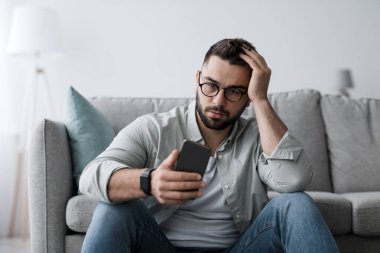 Hata gönderme, kötü haber, ilişkilerden kaynaklanan stres ve kalp kırıklığı. Hayal kırıklığına uğramış bin yıllık gözlüklü adam yere oturup telefona bakar ve iç mekanda kafa kafaya sıkışır.