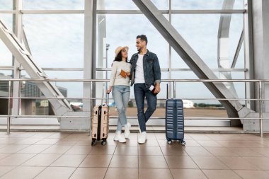 Balayı seyahatleri. Havalimanında bavullarıyla bekleyen romantik genç Arap çift, Panoramik Pencere 'nin yanında uçmayı bekleyen mutlu Orta Doğulu adam ve kadın, seyahate hazır, kopyalama alanı