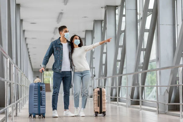 Havalimanında durup yan yana duran koruyucu maskeli Arap çift, Terminalde uçuş bekleyen, Coronavirus salgını sırasında seyahat eden, Boşluğu Kopyalayan Orta Doğulu eşler,