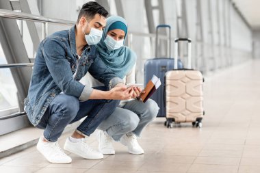 Havaalanında uçuşlarını beklerken akıllı telefon kullanan, tıbbi maske takan Müslüman çift, tersanede bavullarıyla oturan ve cep telefonuyla interneti tarayan genç Müslüman eşler,