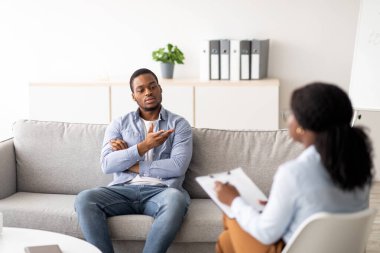 Depresyon tedavisi ve duygusal bozukluklar. Profesyonel psikolog zenci erkek hastaya yardım ediyor, mutsuz Afrikalı Amerikalı bir adamla çalışıyor, klinikte destek ve yardım sağlıyor.