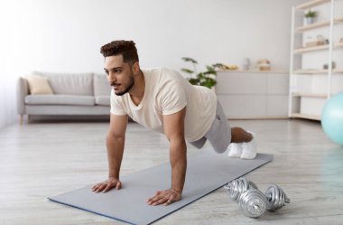 Genç Arap adam tahta duruşunda duruyor ya da şınav çekiyor, evde çalışıyor. Formda bir Orta Doğulu kaslarını çalıştırıyor, koronavirüs kilitlenmesi sırasında vücut geliştirme sorunu yaşıyor.
