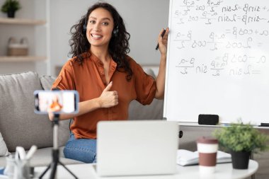 Bayan öğretmen online okulu tavsiye ediyor, işaret gösteriyor, sanal ders veriyor, matematiği anlatıyor. Eğitim hizmetlerinden memnun olan, cep telefonuyla video kaydeden,