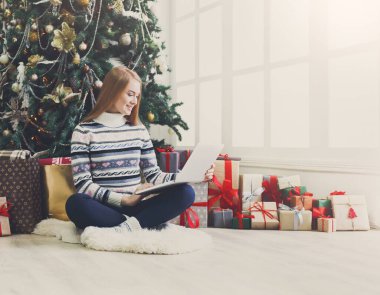 Genç kadın alışveriş online laptop rahat Noel iç. Sürü sarılmış hediye arasında süslü çam ağacının altında rahat oturan kız. Xmas, bying kış satış için hazırlanıyor. Kopya alanı