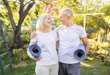 Yoga minderleri tutan, bahçelerinde birlikte egzersiz yapan, kucaklaşan ve birbirine bakan, uzayı kopyalayan mutlu yaşlı eşler.