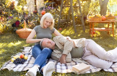 Son sınıf çifti birlikte eğleniyor, bahçede piknik battaniyesinde dinleniyor ve sohbet ediyor, adam karısının bacaklarının üzerinde yatıyor. Mutlu emeklilik kavramı