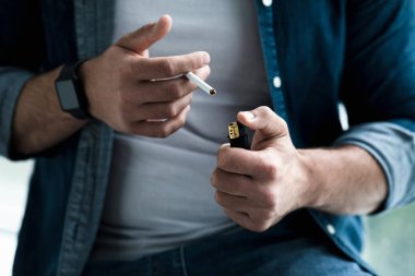 Evde sigara içen bir adam. Nikotin bağımlılığı, zihinsel sorunlar ve sorunlar, kötü alışkanlık ve endişe. Üzücü mutsuz Avrupalı adam sigara yakıyor, kırpıyor, kapıyor, boşluğu dolduruyor.