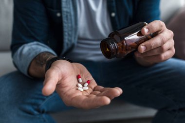 Erkek hastaların avuçlarında bir avuç dolusu beyaz hap. Sağlık, tedavi, uyuşturucu ve depresyon, acı ve intihar. Hüsrana uğramış üzgün genç adam evde antidepresanları elinde tutuyor. Kapatın, kırpın.