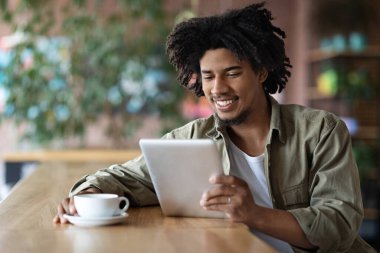 Kafe 'de dijital tablet ve kahveyle rahatlayan genç Afrikalı Amerikalı adam sosyal medyaya göz gezdiren ya da kafeteryada dinlenirken modern Gadget' ta haber okuyan siyah adam.