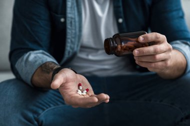 Aşırı doz ve intihar, ruhsal çöküntü, derin depresyon, ilaçlar, ağrı kesiciler ve sağlık sorunları. Üzgün üzgün genç adam elinde kavanozdan farklı haplar dolduruyor, kırpıyor, kapıyor.
