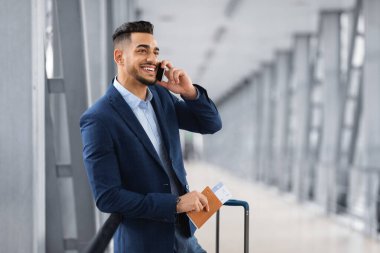 Havaalanı salonunda beklerken cep telefonuyla konuşan yakışıklı Orta Doğulu işadamı, başarılı bir Arap girişimci, Terminal ve Keyifli Cep Telefonu Konuşması 'nda valiziyle duruyor, Boşluğu Kopyala