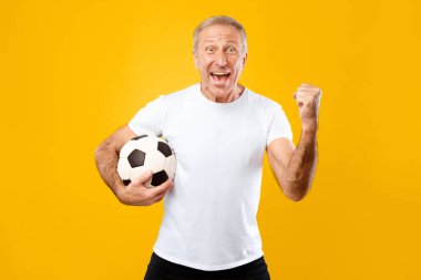Sarı arka planda elinde futbol topu tutan bir adam var. O yaygın bir şekilde gülümsüyor ve kutlama için yumruğunu kaldırdı. O, futbolda bir anlık başarının tadını çıkarıyor gibi görünüyor..