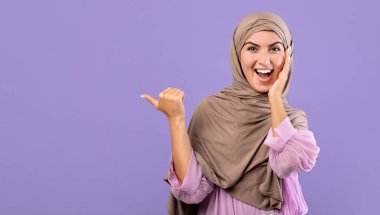 Vay canına, şuna bak. Heyecanlı Ermeni Müslüman kadın mor arka planda, stüdyo çekimlerinde, panoramada boş alana işaret ediyor. Şaşırmış İslamcı kadın senin metin ya da tasarımın için boş yer gösteriyor.