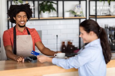 Bin yıllık Afro-Amerikan Kıvırcık Erkek Garson müşterisine taze kahve veriyor. Tatmin olmuş kadın da kafenin içindeki barın girişinde terminal ve kredi kartıyla ödeme yapıyor. İyi hizmet, iş.