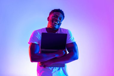 Canlı, neon ışıklı bir mekanda, neşeli bir siyah adam boş bir ekranla dizüstü bilgisayarı kucaklıyor. Bu an, bir web sitesi reklamı için mükemmel olan teknoloji tutkusunu yakalıyor..