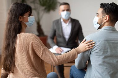 Evlilik Terapisi Konsepti. Mutlu çift terapist ofisinde uzlaşıyorlar, birbirlerine bakıyorlar, gülümseyen kadın erkeğin omzuna dokunuyor. Koruyucu tıbbi maske takan insanlar.