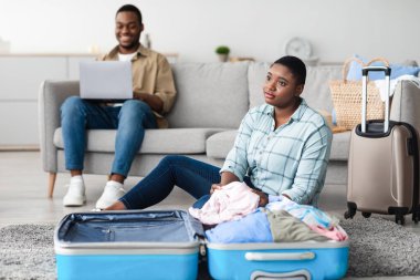 Afrika kökenli Amerikalı Eş Seyahat Bavulu hazırlarken Koca da dizüstü bilgisayarla interneti tarıyor ve online bilet alıyor. Seçici Odaklanma Siyahi Kadın Tatili Düşlüyor