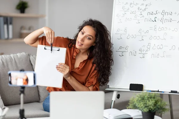 Yeni Tema Açıklanıyor. Sanal konferans yapan genç bayan öğretmen portresi, tripoda cep telefonu kullanan öğrencilere çevrimiçi ders veriyor. Boş kağıda bakan kadın, webcam 'e gösteriyor