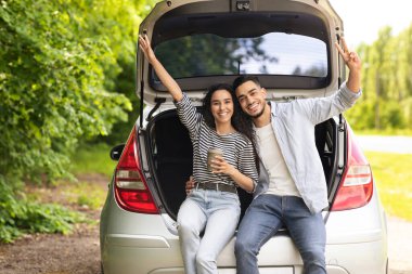 Duygusal ortadoğulu çift kırsal bölgede kahve içiyor, açık bir araba bagajında oturuyor, kucaklaşıyor ve el kol hareketi yapıyor, araba gezintisi yaparken kahve molası veriyor, tatilin tadını çıkarıyor, fotokopi çekiyor.