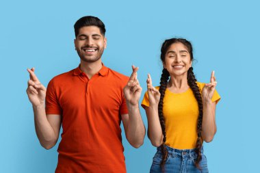 İki genç yetişkin, bir kadın ve bir erkek, yüzlerinde tebessümle yan yana durur, umut ya da iyi şans için parmaklarını çaprazlarlar..