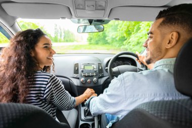 Çok ırklı çiftin el ele tutuşması ve rahat bir arabada otururken birbirlerine gülümsemesi. Mutlu Arap adam güzel kız arkadaşıyla araba gezisine çıkıyor, yaz tatili konsepti.