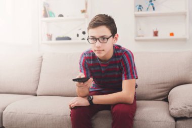 Televizyon izlerken, evde oturma odasında kanepede otururken Tv uzaktan kumanda ile genç çocuk