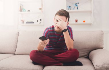 Korkmuş genç gerilim TV izliyor. Çocuk korktuğumu gördüklerini, gözleri el ile kapatma ama throug parmak meraklı. Tek başına oturmak koltukta evde, uzaktan kumanda holding