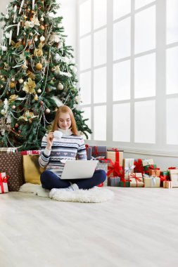 Yılbaşında internetten kahve alışverişi yapan genç bir kadın. Bir sürü hediye arasında süslenmiş köknar ağacının altında oturan kız. Xmas 'a hazırlanmak, kış satışlarında hile yapmak, kopyalama alanı