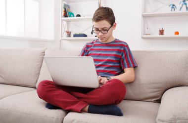 Bilgisayar evde kanepe üzerinde ciddi bir çocuk. Çocuk İnternet, klavyede yazarak dalmış