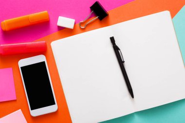 Canlı bir çalışma alanı boş bir defter, renkli kalemler, yapışkan notlar, akıllı telefon ve kalem içerir. Yazmak ya da beyin fırtınası yapmak için davetkar bir atmosfer yaratır..