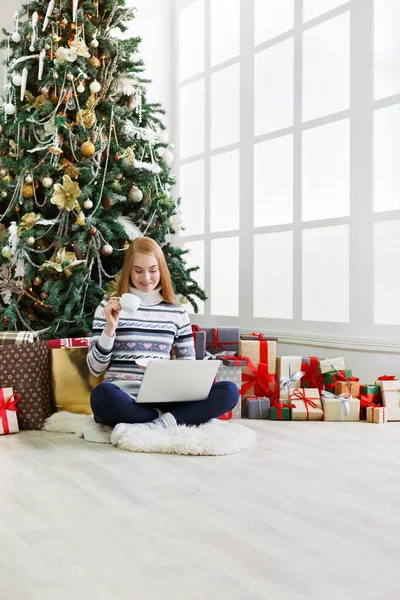 Yılbaşında internetten kahve alışverişi yapan genç bir kadın. Bir sürü hediye arasında süslenmiş köknar ağacının altında oturan kız. Xmas 'a hazırlanmak, kış satışlarında hile yapmak, kopyalama alanı