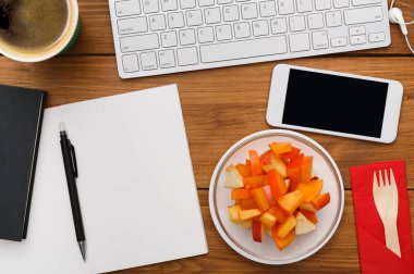 İş yerinde sağlıklı bir iş yemeği. Masaüstü düzlüğü, dizüstü bilgisayar, not defteri, ahşap masa arkasında meyve salatası atıştırmalığı tabağı, hiç kimse, nesneler.