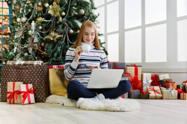 Yılbaşında internetten kahve alışverişi yapan genç bir kadın. Bir sürü hediye arasında süslenmiş köknar ağacının altında oturan kız. Xmas 'a hazırlanmak, kış satışlarında hile yapmak, kopyalama alanı
