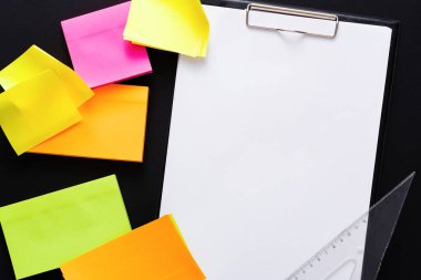 Pembe, sarı ve turuncu tonlarda çeşitli renkli yapışkan notlar siyah bir masanın üzerindeki boş bir panonun etrafını sarıyorlar. Yakınlarda bir cetvel var. Beyin fırtınası ve planlama için mükemmel bir çalışma alanı..